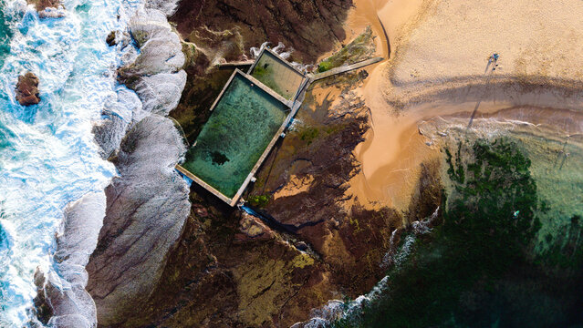 Aerial view of the Mona Vale Rock Pool surrounded by rocky coastline, crashing ocean waves, and sandy beach in Mona Vale, New South Wales, Australia.