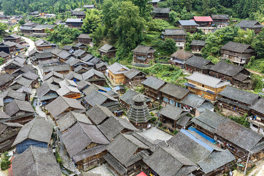 Aerial view of Zaidang Dong Village featuring traditional wooden stilt houses with grey tiled roofs and a central drum tower nestled in a lush mountainous landscape in Guizhou, China.