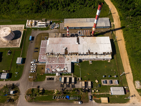 Aerial view of the Tinian power station featuring industrial buildings, tall chimneys, and storage tanks surrounded by lush vegetation in San Jose, Tinian, Northern Mariana Islands.