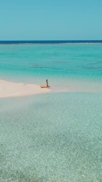 Woman walks gracefully on a white sand beach in the maldives with a yellow kayak, surrounded by turquoise waters and clear blue skies, creating a serene tropical paradise