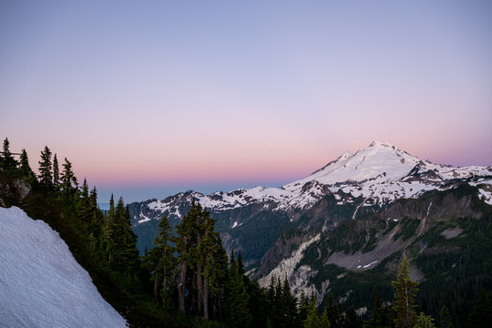 View of Mount Baker at Artist Point with snow-covered slopes, evergreen trees, and a soft purple sunset sky in Deming, Washington, United States.