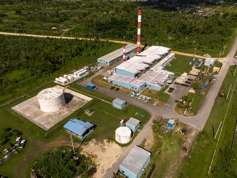 Aerial view of the Tinian power station featuring industrial buildings, tall smokestacks, and storage tanks surrounded by lush greenery in San Jose, Tinian, Northern Mariana Islands.