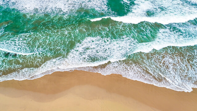 Aerial view of turquoise ocean waves crashing onto the sandy beach in Indonesia.