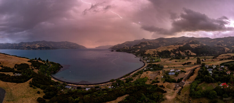 Aerial view of Akaroa Harbour during a storm with dramatic lightning strikes over the water, rolling hills, and coastal landscape, Canterbury Region, New Zealand.