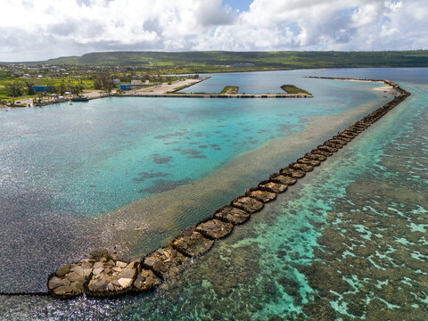 Aerial view of Tinian Port and marina with turquoise waters, coral reefs, and a long breakwater structure in San Jose, Tinian, Northern Mariana Islands.