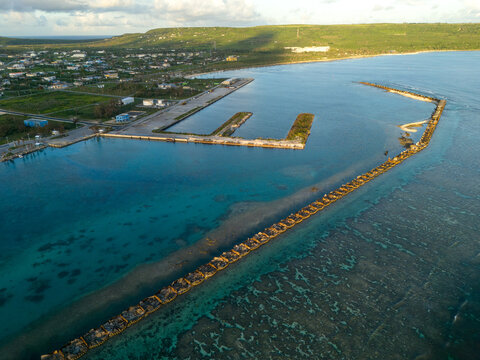 Aerial view of Tinian Port and marina with its long breakwater, clear turquoise waters, and the coastal town in the background, San Jose, Tinian, Northern Mariana Islands.