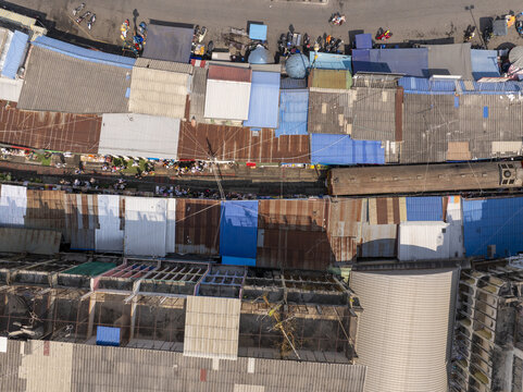 Aerial view of Maeklong Railway Market with colorful awnings and metal rooftops lining the train tracks in Mae Klong, Samut Songkhram, Thailand.