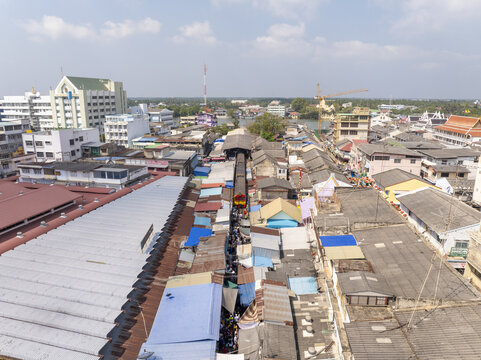 Aerial view of Maeklong Railway Market with a train passing through the narrow market stalls, surrounded by dense urban rooftops in Mae Klong, Samut Songkhram, Thailand.