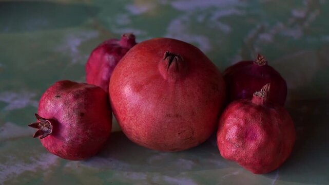 Slow motion camera panning of a group of whole red pomegranates on a green textured surface, horizontal video.