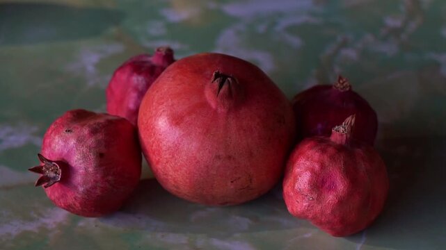 Slow motion camera panning of a group of whole red pomegranates on a green textured surface, horizontal video.