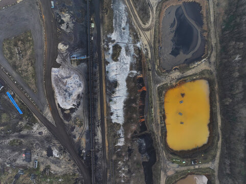 Aerial view of an industrial site featuring settling ponds with yellow and dark water, surrounded by dirt tracks and industrial infrastructure in Germany.