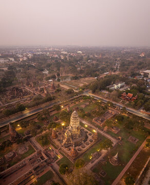 Aerial view of Wat Ratchaburana with its central prang, surrounding ancient ruins, lush trees, and illuminated pathways at dusk in Amphoe Phra Nakhon Si Ayutthaya, Chang Wat Phra Nakhon, Thailand.