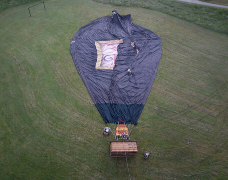 Aerial view of a deflated hot air balloon lying on a green grassy field with its wicker basket and black fabric envelope spread out in the Netherlands.