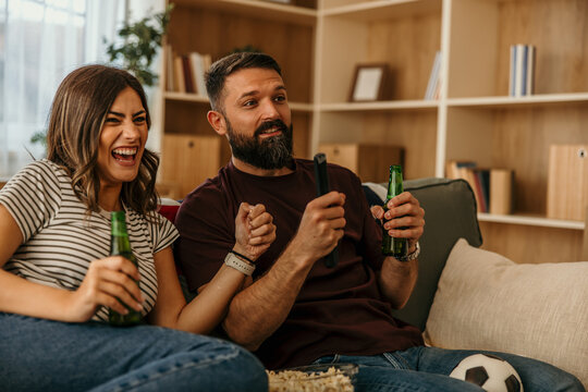 Couple watching soccer game at home cheering with beer