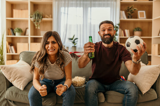 Couple watching soccer game together with contrasting emotions