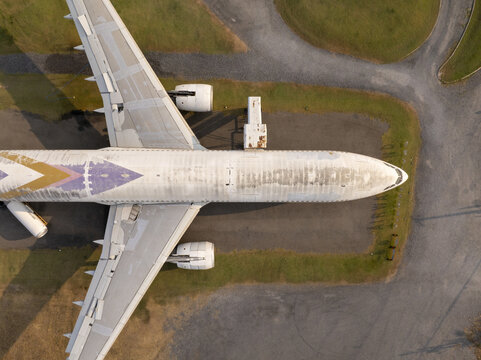 Aerial view of a weathered airplane parked on an asphalt surface surrounded by grass in Thailand.