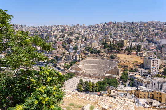 View of the historic Roman Theater nestled within the urban landscape of Amman, featuring stone seating tiers and a large plaza in Amman, Amman Governorate, Jordan.