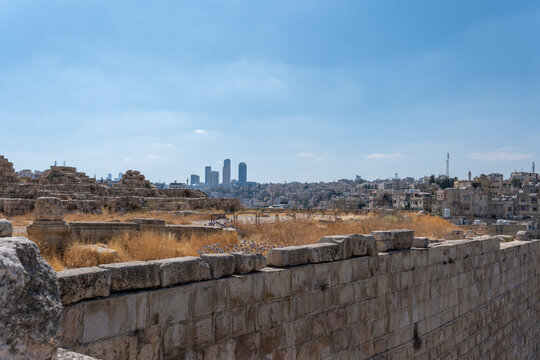 View of the historic Umayyad Palace ruins with dry grass and stone walls in the foreground, overlooking the modern city skyline of Amman, Amman Governorate, Jordan.