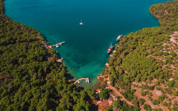 Aerial view of Telascica Nature Park featuring a turquoise bay surrounded by dense pine forests and docked boats in Sali, Zadar County, Croatia.