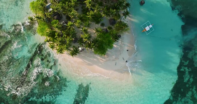 Aerial view of Guyam Island featuring lush palm trees, white sand beach, and a traditional outrigger boat floating in turquoise water in General Luna, Caraga, Philippines.