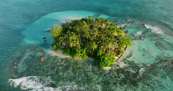 Aerial view of Guyam Island featuring lush palm trees, white sand beaches, and vibrant coral reefs surrounded by clear turquoise water in General Luna, Caraga, Philippines.