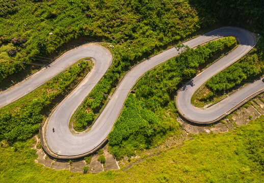 Aerial view of the winding Doc Tham Ma road surrounded by lush green mountains and dense vegetation in Pho Bang, Tuyen Quang, Vietnam.