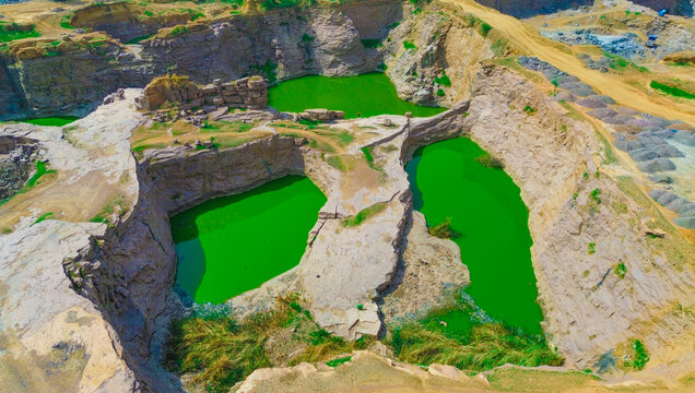 Aerial view of the Kano City quarry featuring deep pits filled with vibrant green water, surrounded by rugged rock formations, arid terrain, and sparse vegetation in Kano, Kano, Nigeria.