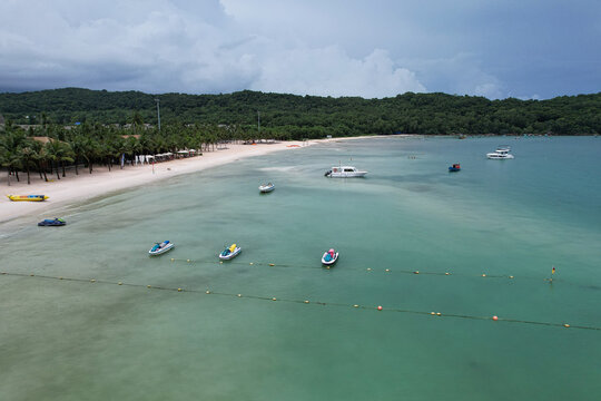 Aerial view of Khem Beach with turquoise water, white sand, palm trees, and various boats and jet skis moored along the coastline in Phu Quoc, Kien Giang, Vietnam.