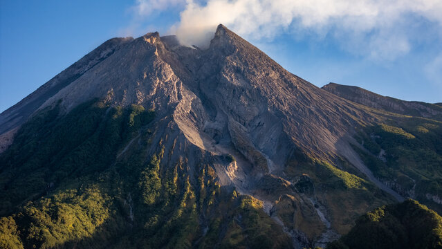 Aerial view of Bukit Klangon overlooking the active Mount Merapi volcano with rocky slopes, smoke, and green vegetation in Kecamatan Cangkringan, Daerah Istimewa Yogya, Indonesia.