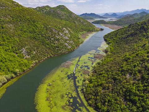 Aerial view of Pavlova Strana showing the winding Rijeka Crnojevica river flowing through lush green hills and dense forests in Prijestonica Cetinje, Montenegro.