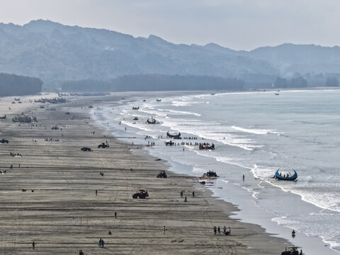 Cox's Bazar, Chittagong Division, Bangladesh - 10 April 2026: Aerial view of Cox's Bazar Sea Beach with traditional fishing boats, people on the sand, and tractors along the shoreline.
