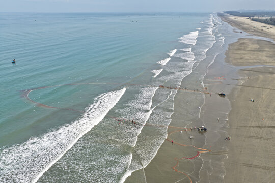 Cox's Bazar, Bangladesh - 10 April 2026: Aerial view of Cox's Bazar Sea Beach with fishermen pulling large nets from the surf, sandy coastline, and calm blue sea.