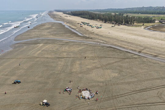Cox's Bazar, Bangladesh - 10 April 2026: Aerial view of Cox's Bazar Sea Beach with wooden fishing boats, a group of fishermen sorting their catch, and tire tracks on the sand.
