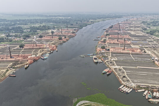 Dhaka, Bangladesh - 12 April 2026: Aerial view of brick kilns lining the riverbanks with smoking chimneys and rows of drying bricks in Dhaka, Bangladesh.