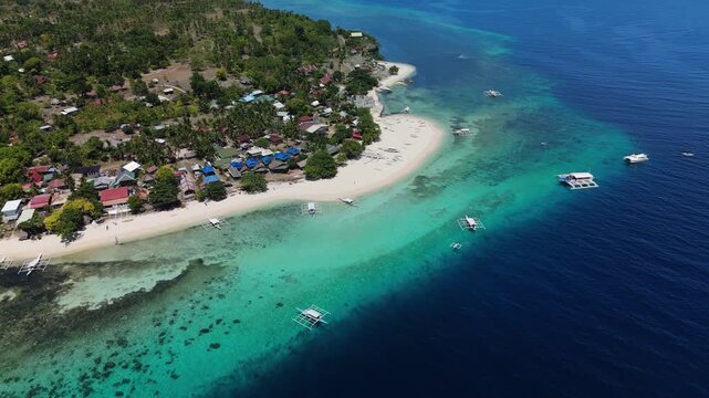 Aerial view of Panglao beach with turquoise water, traditional outrigger boats, and coastal village houses in Panglao, Central Visayas, Philippines.