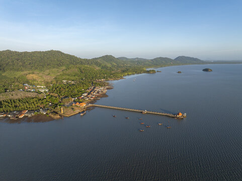 Aerial view of Lanta Old Town with its long wooden pier extending into the sea, surrounded by lush green hills and coastal vegetation in Ko Lanta Yai, Krabi, Thailand.