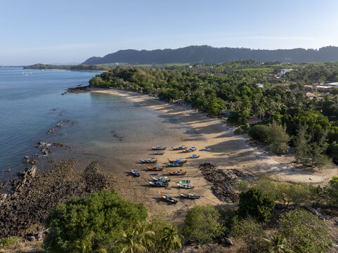 Aerial view of Secret Beach with traditional long-tail boats resting on the sandy shore, surrounded by lush tropical greenery and rocky formations along the coastline in Ko Lanta, Thailand.