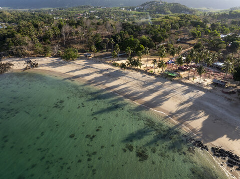 Aerial view of Secret Beach with turquoise waters, sandy shore, and palm trees in Ko Lanta, Thailand.