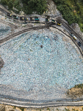 View of a large landfill site with trucks driving on a dirt road surrounded by waste in Denpasar, Bali, Indonesia.