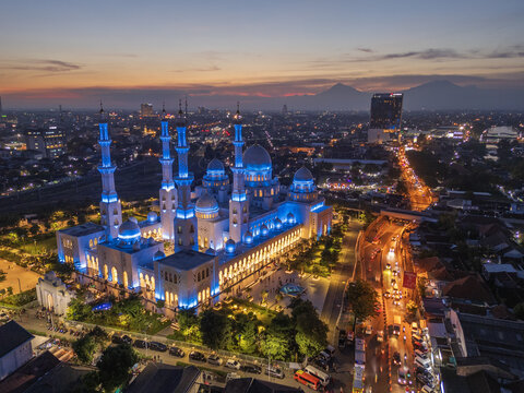 Kecamatan Banjarsari, Indonesia - 23 October 2024: Aerial view of Sheikh Zayed Grand Mosque Solo Surakarta illuminated at night, surrounded by urban streets and traffic under a sunset sky.