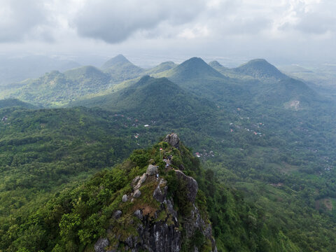 Kecamatan Sampung, Indonesia - 25 May 2025: Aerial view of Bukit Cumbri with its rocky peak, lush green forested hills, and cloudy sky in the background.