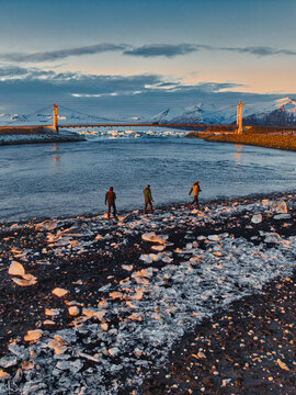 Aerial view of Diamond Beach with ice chunks scattered on the black sand shore and people walking near the bridge in Hofn, Sveitarfelagid Hornaf, Iceland.