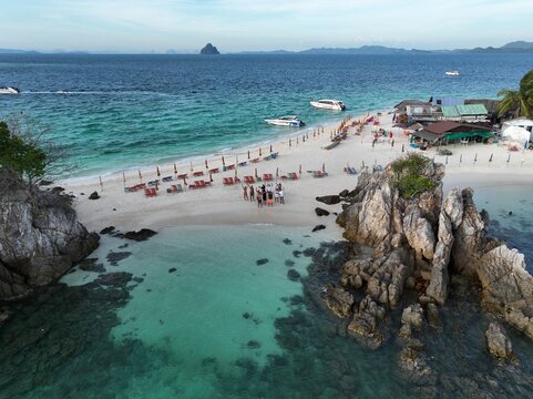 Aerial view of Koh Khai Nok beach with turquoise waters, rocky outcrops, speedboats, and people standing on the white sand in Phru Nai, Phang Nga, Thailand.