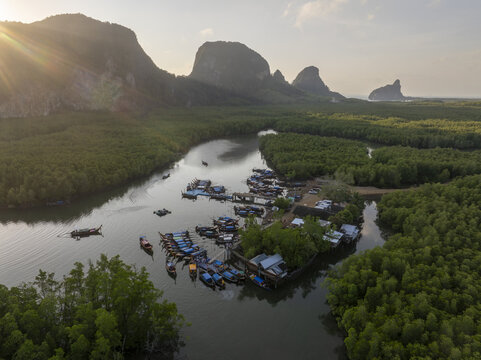 Aerial view of Hin Rom Pier with long-tail boats in the mangrove forest, near limestone karst mountains during golden hour in Tambon Khlong Khian, Chang Wat Phang-nga, Thailand.