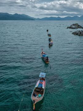 Aerial view of a line of traditional long-tail boats floating on the turquoise sea near the rocky Ko Hin Ngam Noi island in Ko Tarutao, Satun, Thailand.