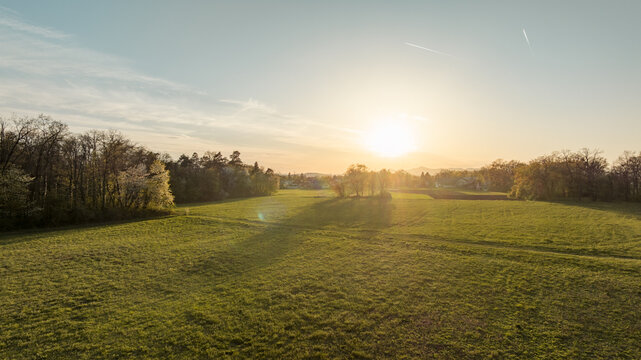 Aerial view of Zajcja dobrava forest and green fields at sunset with warm golden light, trees, and clear sky in Ljubljana - Polje, Ljubljana, Slovenia.