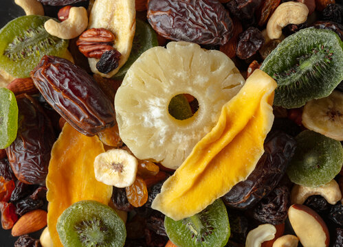 Dried tropical fruits, nuts, and raisins in black plate.
