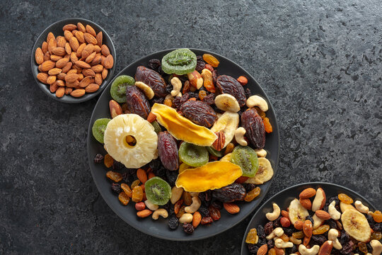 Dried tropical fruits, nuts, and raisins in black plate.