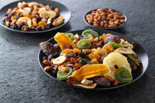Dried tropical fruits, nuts, and raisins in black plate.