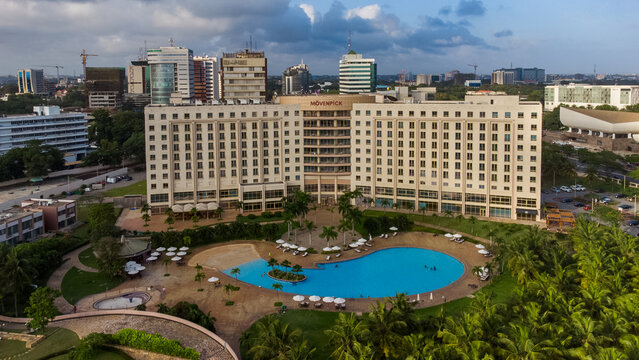 Accra, Ghana - 25 August 2021: Aerial view of Movenpick Ambassador Hotel Accra with its large swimming pool, lush gardens, and surrounding urban skyline under a cloudy sky.